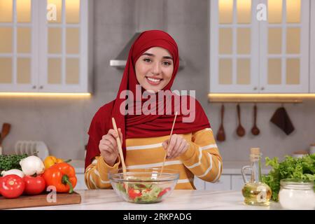 Donna musulmana che prepara una deliziosa insalata con verdure al tavolo bianco in cucina Foto Stock