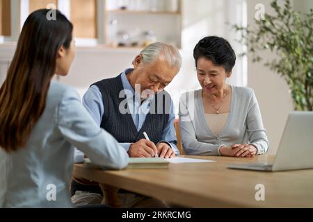 senior asian couple signing an agreement in front of a saleswoman at home Stock Photo