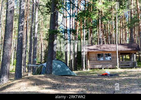 Una tenda e un cottage nel mezzo della pineta vicino al lago Valgojarv nell'area protetta di Meenikunno in una soleggiata mattinata estiva, Estonia Foto Stock