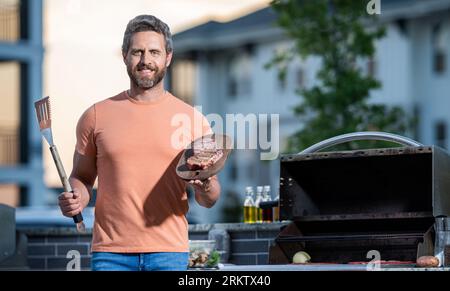 cuoco che mostra le sue tecniche di barbecue durante l'evento di cucina. Uomo che si diverte a fare barbecue. uomo che grigia le sue carni preferite. Grill maestro di arte culinaria, c Foto Stock