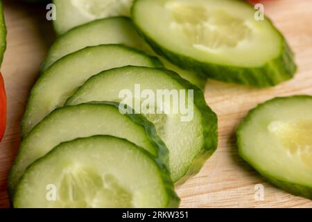 Cetriolo lungo verde a fette durante la preparazione dell'insalata, preparazione dell'insalata con verdure tagliate a pezzetti di cetrioli verdi Foto Stock