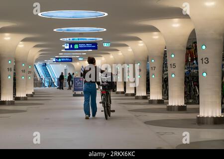 La vista posteriore di donna porta la sua bici dal parcheggio sotterraneo multipiano della stazione centrale di Amsterdam, Olanda Foto Stock