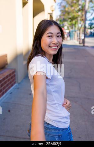 Giovane donna asiatica che guarda indietro e raggiunge la mano per tenere in mano | marciapiede in centro Foto Stock