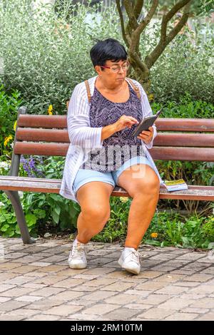 Donna seduto sul panchina del parco del centro città a controllare i messaggi dello smartphone - Tours, Indre-et-Loire (37), Francia. Foto Stock