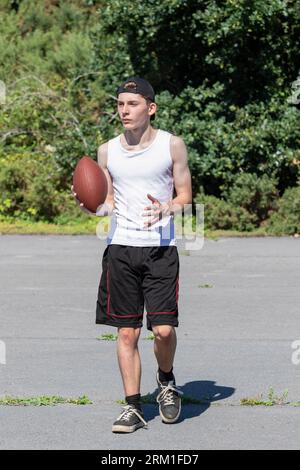 Ragazzo in forma e attivo che lancia in giro un football americano Foto Stock