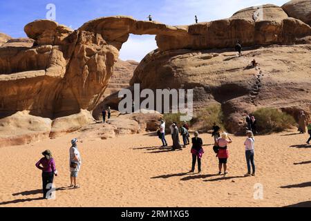 Turisti al ponte di roccia Burdah, al Wadi Rum, sito patrimonio dell'umanità dell'UNESCO, in Giordania, Medio Oriente Foto Stock