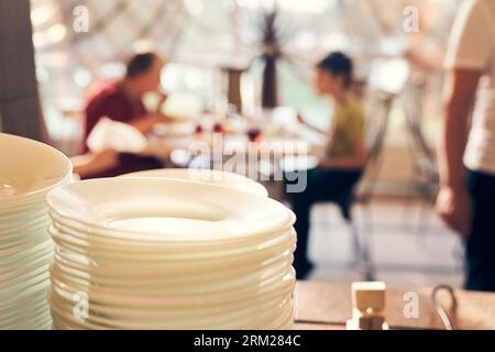 Pile di lastre bianche vengono distribuite sullo sfondo delle persone alla finestra. Vista del ristorante dal tavolo con la distribuzione dei piatti. Foto di alta qualità Foto Stock