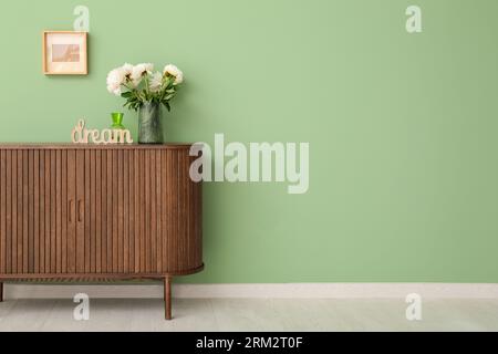 Vaso di peonie bianche e decorazioni a forma di SOGNO DI parole su comò vicino alle pareti verdi Foto Stock