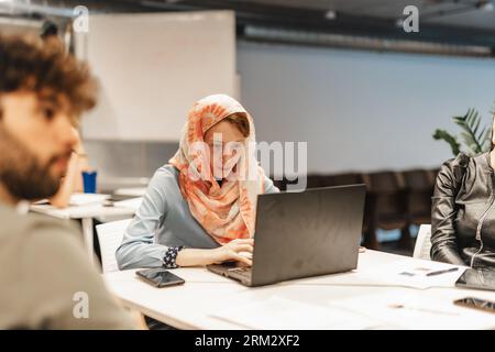 Bellissima zenzero in hijab che lavora su un computer portatile e risolve le attività quotidiane al lavoro. Dipendente femminile concentrato nell'hijab che lavora sul laptop. Foto Stock