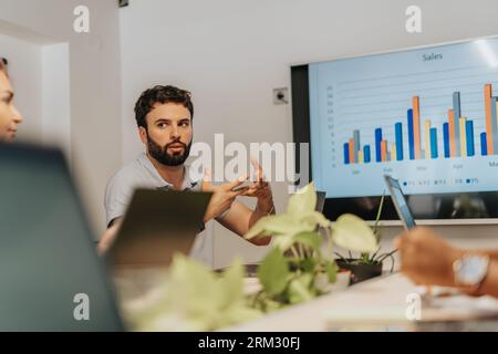 In questo diversificato ufficio indoor, un team aziendale multiculturale collabora in modo creativo su un computer, concentrandosi sull'analisi delle statistiche e sulla discussione delle pubbliche relazioni Foto Stock