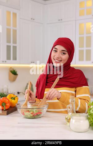 Donna musulmana che prepara una deliziosa insalata con verdure al tavolo bianco in cucina Foto Stock