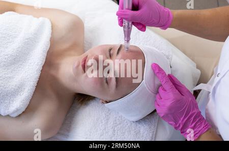 Top View cosmetologo che fa iniezione di mesoterapia con Dermapen sul viso di giovane donna per ringiovanimento nel centro termale. Paziente che riceve ago Foto Stock