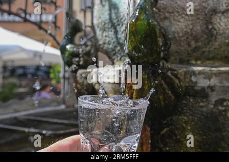 Stoccarda, Germania. 24 agosto 2023. Alla fontana Hans-IM-Glück nel centro di Stoccarda, un bicchiere d'acqua è riempito di acqua potabile. La fontana è una delle 106 fontane per bere e 13 fontane minerali nella capitale dello stato del Baden-Württemberg. (A dpa "Basic Foodstuff potabile water - Municipalities up more Fountains") crediti: Bernd Weißbrod/dpa/Alamy Live News Foto Stock