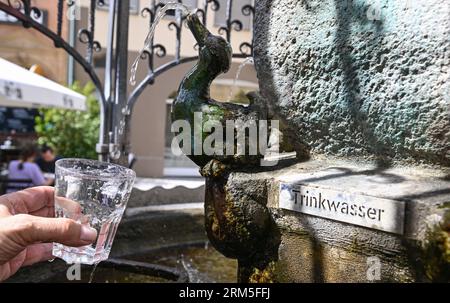 Stoccarda, Germania. 24 agosto 2023. Alla fontana Hans-IM-Glück nel centro di Stoccarda, un bicchiere d'acqua è riempito di acqua potabile. La fontana è una delle 106 fontane per bere e 13 fontane minerali nella capitale dello stato del Baden-Württemberg. (A dpa "Basic Foodstuff potabile water - Municipalities up more Fountains") crediti: Bernd Weißbrod/dpa/Alamy Live News Foto Stock