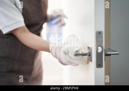 Donna asiatica che sterilizza le maniglie delle porte con l'alcol Foto Stock