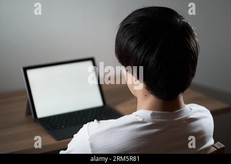 Un uomo asiatico che si dirige verso un portatile nel cuore della notte Foto Stock