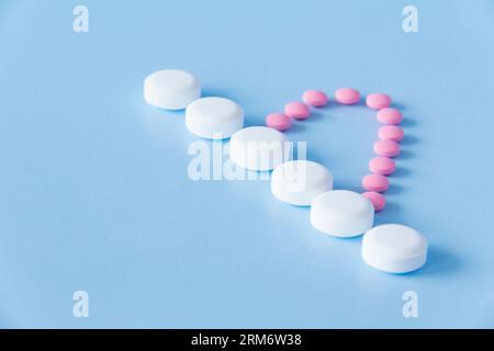 Mezzo cuore di medicine rosa e una linea bianca di grandi pillole bianche su sfondo blu. Il concetto di uno stile di vita sano e medico tempestivo Foto Stock