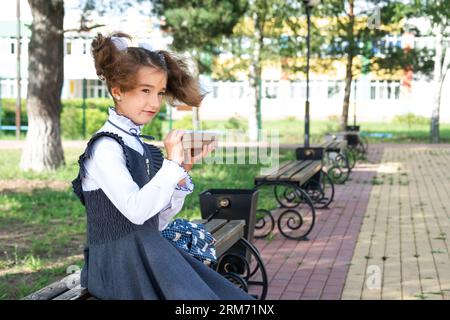 Ragazza con zaino che mangia panino confezionata in una scatola vicino a scuola. Uno spuntino veloce con un panino, cibo malsano, pranzo da scuola. Torna a scuola. Foto Stock
