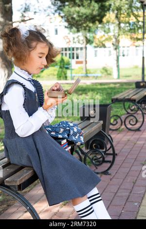 Ragazza con zaino che mangia panino confezionata in una scatola vicino a scuola. Uno spuntino veloce con un panino, cibo malsano, pranzo da scuola. Torna a scuola. Foto Stock