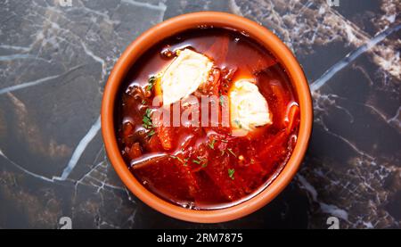 Borscht tradizionale ucraino o russo di verdure rosse e zuppa di carne in vasi di argilla con panna acida su fondo di legno. Vista dall'alto. Foto Stock