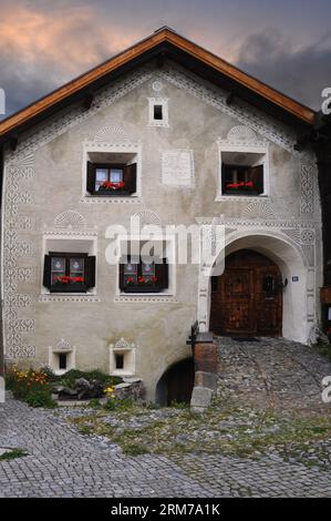 Lingua romena e gerani rossi. Casa tradizionale a Guarda, un villaggio prevalentemente di lingua romansa nella bassa valle dell'Engadina a Graubünden o nel cantone dei Grigioni, in Svizzera. Foto Stock