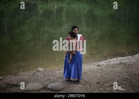 Una donna del gruppo etnico Ngabe Bugle porta il suo bambino in un campo vicino alla riva del fiume Tabasara nella regione indigena Ngabe Bugle, 450 km a ovest di Panama City, capitale di Panama, il 24 febbraio 2014. La regione indigena di Ngabe Bugle si trova nella regione occidentale di Panama e copre un'area di 6.968 km quadrati, con il 91% della sua popolazione che vive in estrema povertà. I leader indigeni della regione di Ngabe Bugle hanno dichiarato un allarme nazionale , a causa dell' avviso di sfratto emesso da una società che sta sviluppando il progetto idroelettrico Barro Blanco . Il progetto userà l'acqua di Taba Foto Stock