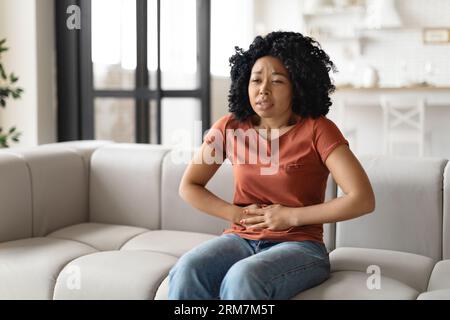 Stomach Ache. Donna Nera malata che soffre di dolore addominale acuto a casa Foto Stock