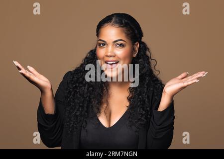 Sorprende una donna brasiliana di taglia extra che alza le mani e guarda la fotocamera con entusiasmo, reagisce all'offerta o alla promozione Foto Stock