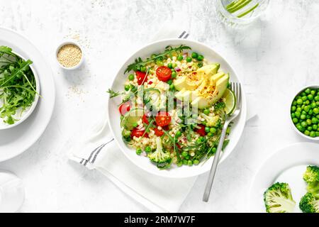 Insalata di couscous con broccoli, piselli verdi, pomodori, avocado e rucola fresca. Cibo vegetariano a base vegetale naturale sano per pranzo, cucina israeliana, Foto Stock