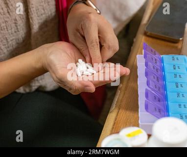 Mani femminili che selezionano pillole in scatole di pillole mediche. Scatola di pillole con le parole Lun-Dom, AM e PM, per alleviare le dosi giornaliere di pillole. Smartphone e bot Foto Stock