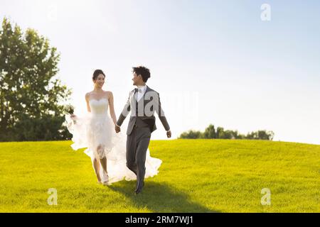 Sposo e sposo felici che corrono sull'erba Foto Stock