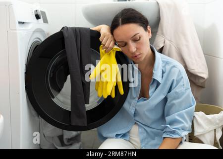Una casalinga stanca si siede vicino alla lavanderia sporca. Routine domestica e lavoro femminile. Foto Stock