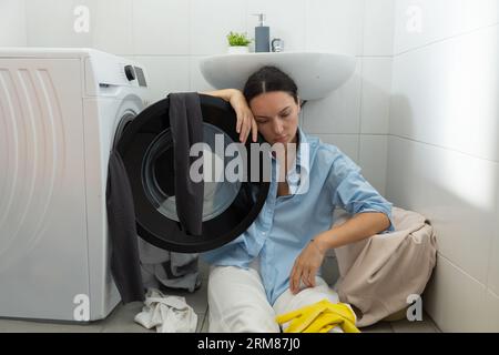 Una casalinga stanca si siede vicino alla lavanderia sporca. Routine domestica e lavoro femminile. Foto Stock