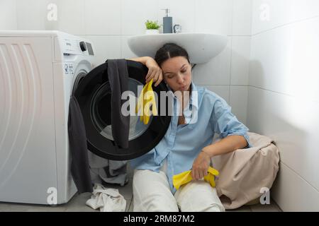 Una casalinga stanca si siede vicino alla lavanderia sporca. Routine domestica e lavoro femminile. Foto Stock