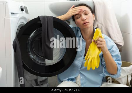 Una casalinga stanca si siede vicino alla lavanderia sporca. Routine domestica e lavoro femminile. Foto Stock