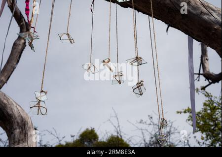 Gruppo simbolico di pezzi di vetro sulle corde e nastro bianco con il cielo e il vecchio albero come sfondo. Astratto, tema decorativo Foto Stock