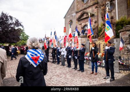 27 agosto 2023, Francia, Pexonne: Una donna indossa una sciarpa di solidarietà con lo schema dell'abbigliamento dei prigionieri nei campi di concentramento tedeschi, il triangolo rosso con la lettera "F" sta per prigionieri politici francesi, durante una cerimonia commemorativa per le vittime dell'invasione di Pexonne il 27 agosto 1944. Alla fine di agosto del 1944, i soldati tedeschi invasero il villaggio francese di Pexonne e rapirono dozzine di abitanti del villaggio. L'azione fu guidata dall'SS-Hauptsturmführer Erich otto Wenger. I nipoti di Wenger sono venuti in città per la prima volta per partecipare a un servizio commemorativo per le vittime del crimine. PH Foto Stock