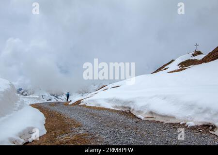 Escursionista solitario nella regione del Montafon delle Alpi austriache, camminando su un sentiero attraverso campi di neve fitta verso la croce in cima al Golmer Joch Foto Stock