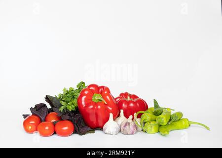 Peperoni, aglio, pomodori, peperoni caldi giacciono su uno sfondo bianco, vengono preparati gli ingredienti per l'adjika, un set di verdure, senza carne Foto Stock