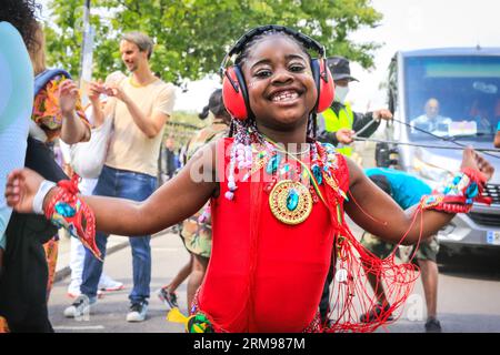 Londra, Regno Unito, 27 agosto 2023. Aliah, una giovane partecipante del gruppo con sua madre, si diverte a ballare alla parata. Gruppo mas Caribbean Sessions e giovani ballerini. Il carnevale di Notting Hill inizia con il carnevale dei bambini e con un percorso per famiglie. Si prevede che fino a due milioni di persone celebrino il carnevale di questo fine settimana festivo partecipando o guardando lungo il percorso del carnevale, presso impianti sonori, bancarelle e locali. Polveri e pitture colorate, in riconoscimento della tradizione caraibica e inizio delle festività del Carnevale di Notting Hill. Foto Stock