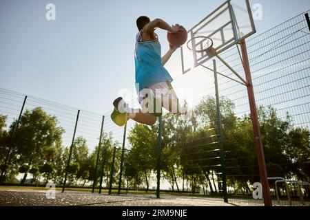 Giocatore adolescente che lancia palla nel canestro da basket, spara in movimento, vista dal basso Foto Stock