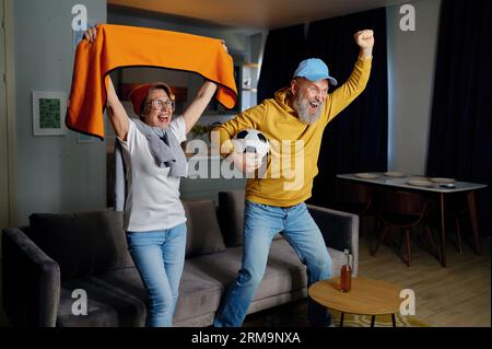 Felice coppia anziana che fa il tifo per guardare le competizioni sportive TV Foto Stock