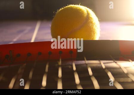Una foto di una palla da tennis gialla accanto a una racchetta da tennis su un tavolo blu. Foto Stock