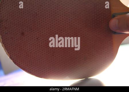 Una foto di una persona che gioca a ping pong con una racchetta da ping pong rossa e nera alla luce. Foto Stock