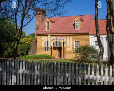 A Colonial Williamsburg, Virginia, una deliziosa casa a due piani presenta vistosi binari gialli, un audace tetto rosso e un importante camino in mattoni. Contro Foto Stock