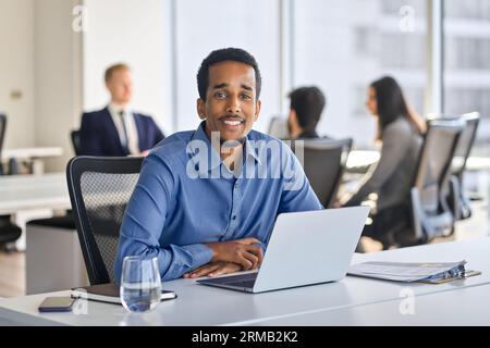 Sicuro e felice giovane uomo d'affari africano seduto al lavoro con un computer portatile. Foto Stock