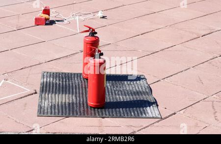 Due estintori manuali grandi in metallo rosso ad anidride carbonica o a polvere per l'estinzione di una base antincendio su un tappeto dielettrico in gomma nera sul pavimento. Foto Stock