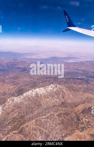 Montagne con neve, cielo blu - vista dal finestrino dell'aereo, ala dell'aereo flydubai - vista aerea da un posto finestrino dell'aereo Foto Stock