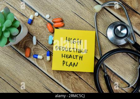 Concetto di piano sanitario ad alta deducibilità scrivere su note adesive con stetoscopio isolato su tavolo di legno. Foto Stock