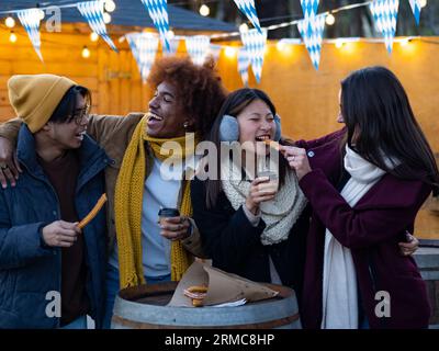 Gruppo di amici diversi in inverno che mangiano churros e cioccolata calda per strada in Spagna Foto Stock